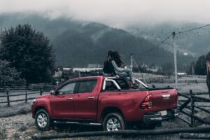 two women sitting on red pickup truck viewing mountain on a foggy day